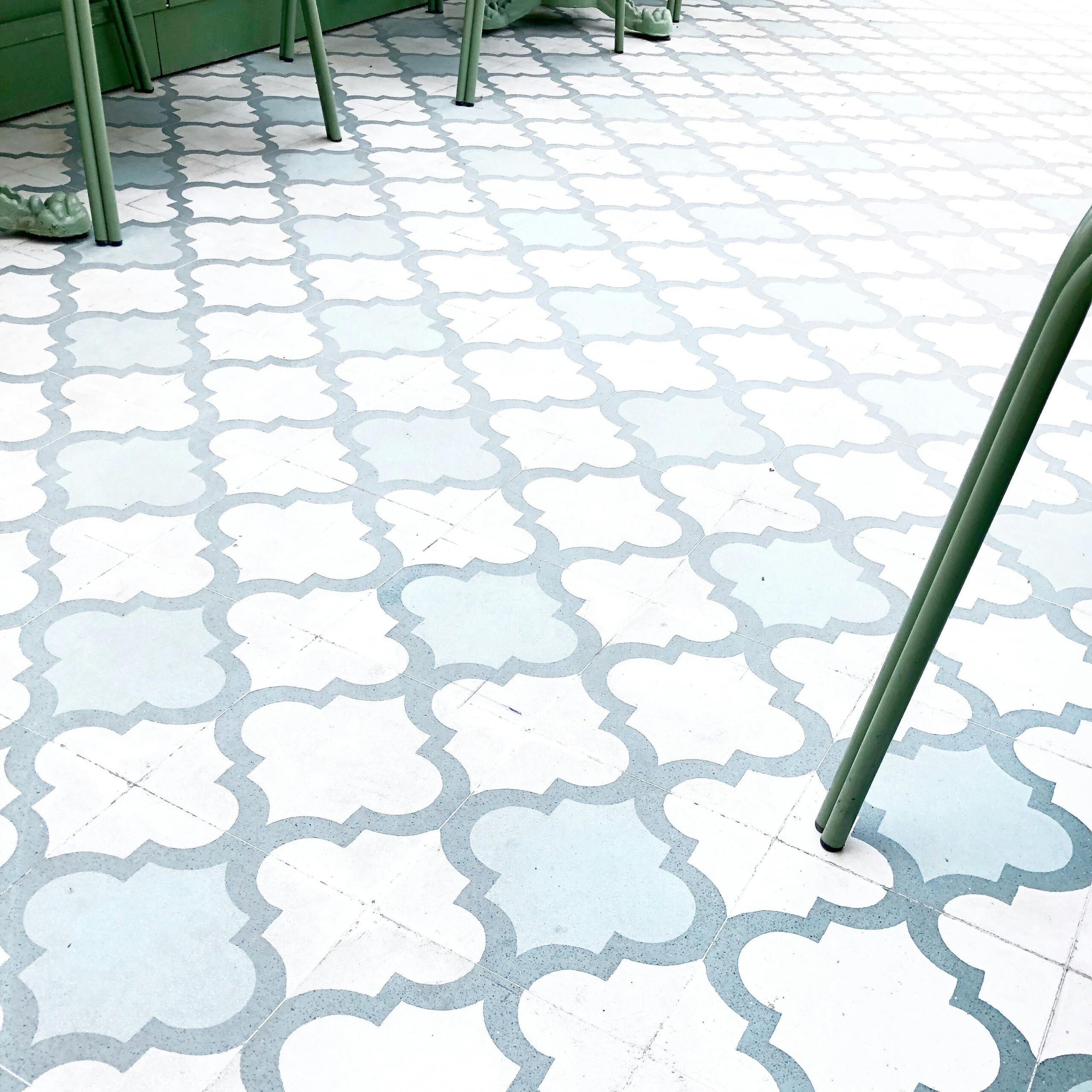 Geometric quatrefoil pattern tiles with green metal furniture legs in a modern setting.